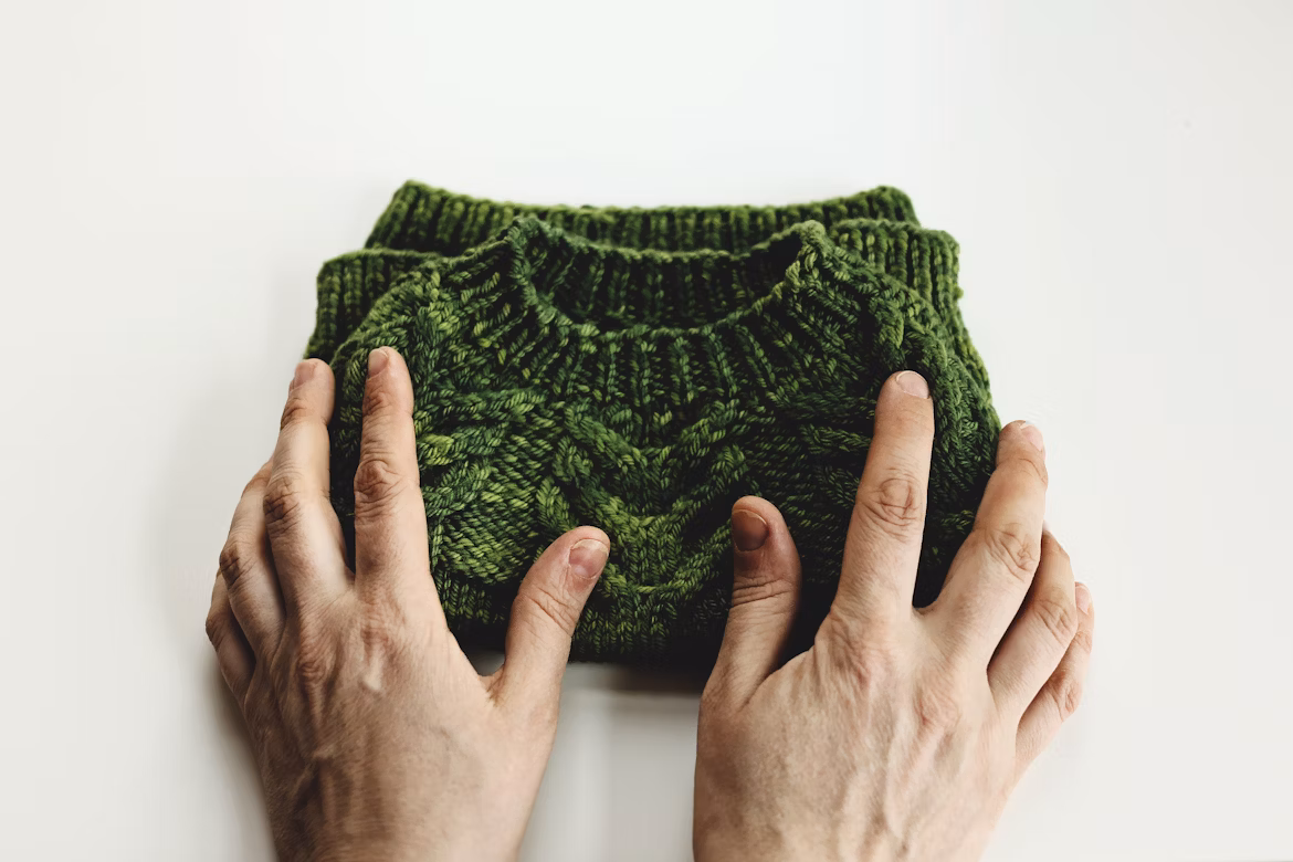 Two hands fold a dark green, knit sweater